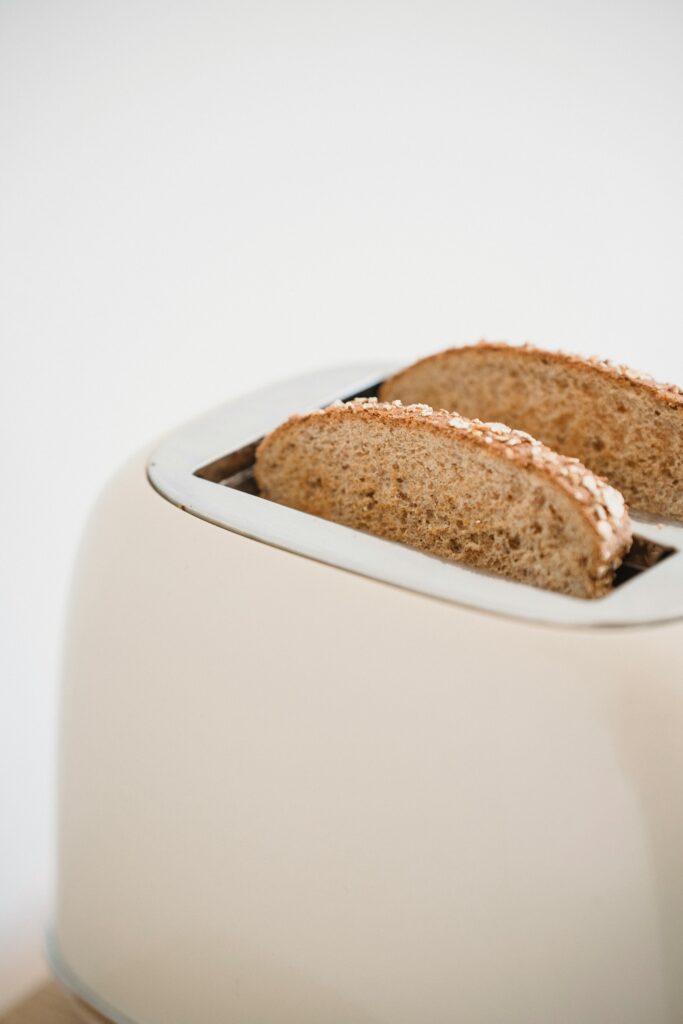Fresh slices of whole-grain bread in a white toaster, minimal kitchen scene.